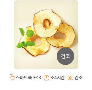 화면의 중앙에 얇게 슬라이스된 사과칩이 위치해 있습니다. 사과칩의 중앙은 동그랗게 잘라져 링 형태로 되어 있습니다. 사과칩은 노르스름하게 잘 건조되어 있으며, 왼쪽 사과칩 위에는 장식하기 위한 녹색의 이파리가 올려져 있습니다. 화면의 오른쪽 하단에는 회색 원안에 “건조” 라고 적혀져 있습니다.
