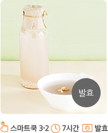 베이지색의 그릇과 유리병이 위치해 있습니다. 앞쪽에 위치한 유리그릇에는 식혜가 담겨져 있으며, 그 위에 잣이 중앙에 띄어져 있습니다. 뒤쪽의 유리병안에도 식혜로 채워져 있으며, 병 입구에는 종이와 노끈으로 밀봉되어 있습니다.화면의 오른쪽 하단에는 회색 원안에 “발효” 라고 적혀져 있습니다.