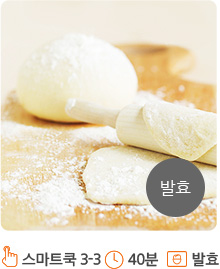 나무테이블위에 빵 반죽들이 놓여져 있습니다. 왼쪽에는 둥근모양의 빵 반죽이, 오른쪽에는 밀대로 밀려져 있는 빵 반죽이 위치해 있습니다. 빵 반죽이 위치한 나무테이블위로는 밀가루가 뿌려져 있습니다. 또한 화면의 오른쪽 하단에는 회색 원안에 “발효” 라고 적혀져 있습니다.