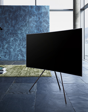 파란색감의 인테리어로 구성이 된 실내중앙에 스튜디오 스탠드가 장착된 QLED TV가 우측으로 비스듬하게 가운데에 세워져 있습니다.