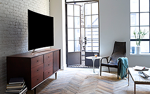 선반위에 올라가져 있는 QLED TV의 측면이 보여지고 있으며 제품의 앞에는 쇼파 및 테이블이 보여집니다.