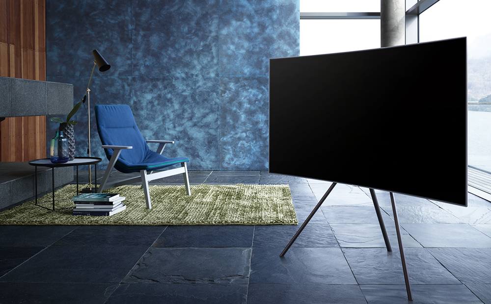 파란색감의 인테리어로 구성이 된 실내중앙에 스튜디오 스탠드가 장착된 QLED TV가 우측으로 비스듬하게 가운데에 세워져 있습니다.