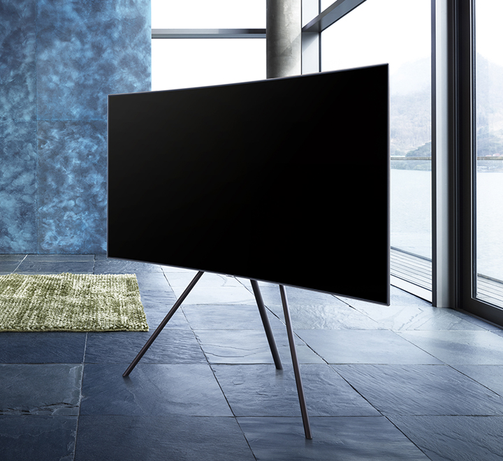 파란색감의 인테리어로 구성이 된 실내중앙에 스튜디오 스탠드가 장착된 QLED TV가 우측으로 비스듬하게 가운데에 세워져 있습니다.