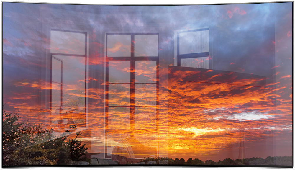 제품의 베젤과 화면만 보여지고 있으며, 화면 안에는 노을진 하늘에 붉은 구름과 파란색 구름이 보여지고 중앙에 가로 선이 있으며 좌측에는 빛이 반사되어 창문이 비추고 있습니다.