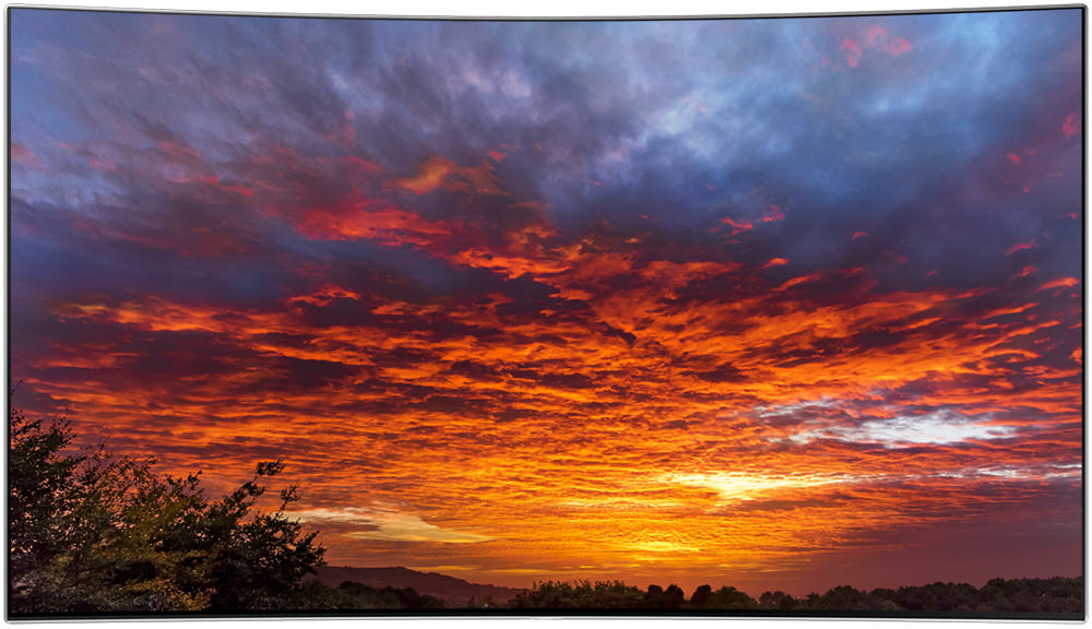 제품의 베젤과 화면만 보여지고 있으며, 화면 안에는 노을진 하늘에 붉은 구름과 파란색 구름이 보여지고 있습니다.