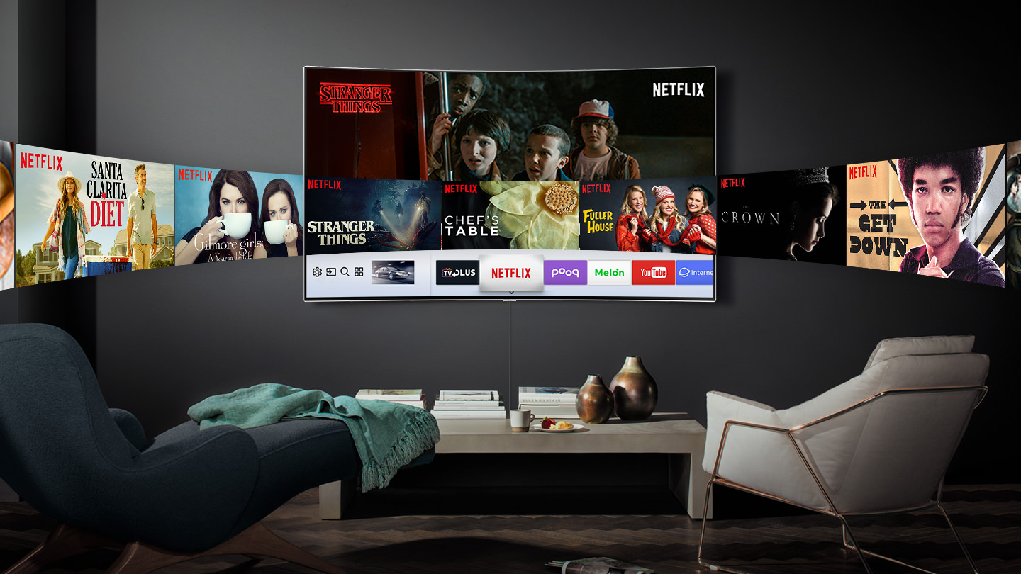 중앙 벽에 QLED TV가 걸려있으며 화면안에는 NETFLIX 이미지와 좌우측으로 NETFLIX에서 방영하는 드라마 및 영화들의 이미지들이 QLED TV를 기준으로 유선형으로 이루어져 있습니다. QLED TV앞쪽에는 작은 선반과 좌측엔 화분, 우측에는 미니 테이블이 있으며 정면에는 의자가 놓여져 있습니다.